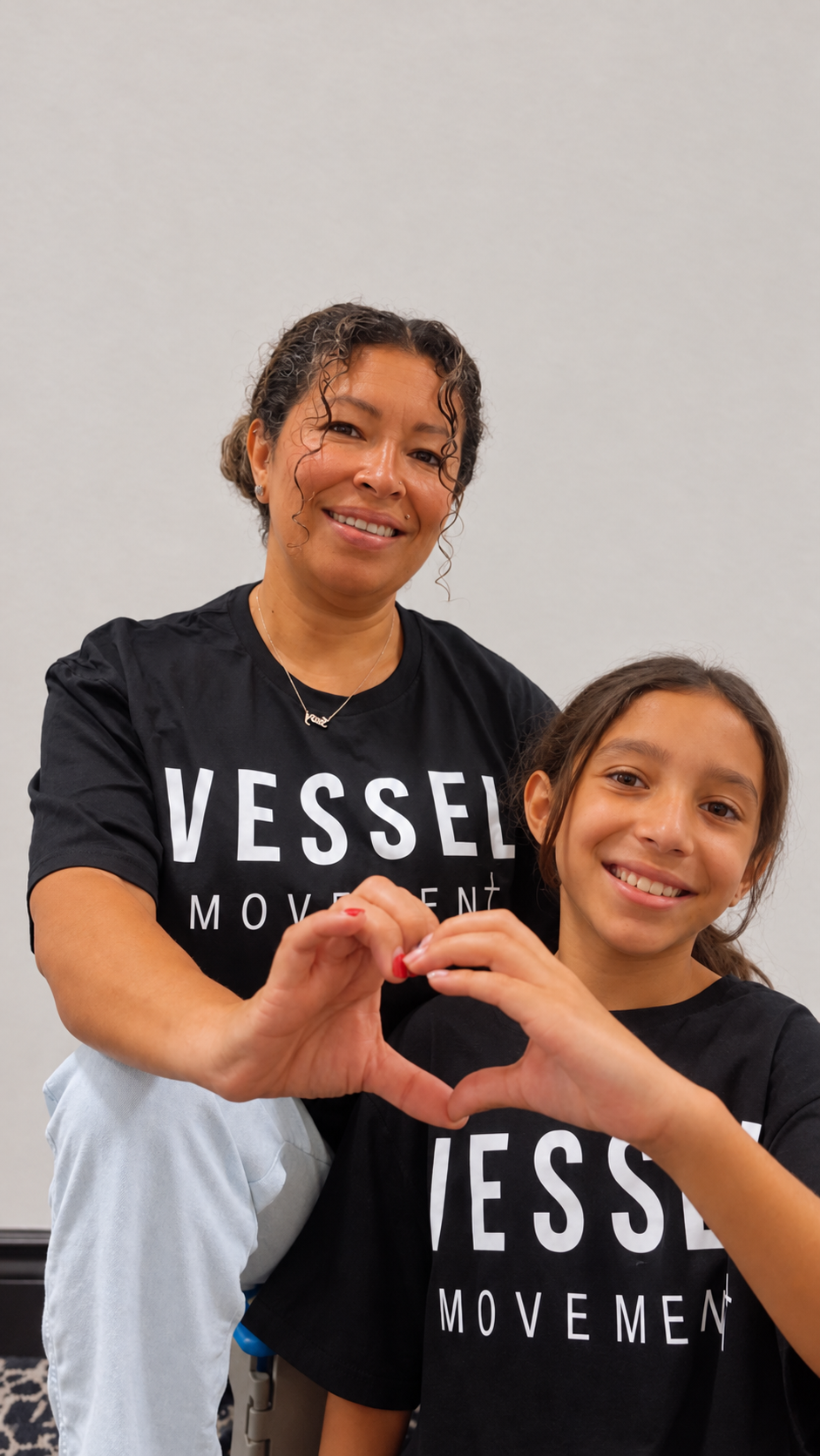 A mother and daughter wearing Vessel Movement shirts and making a heart with their hands