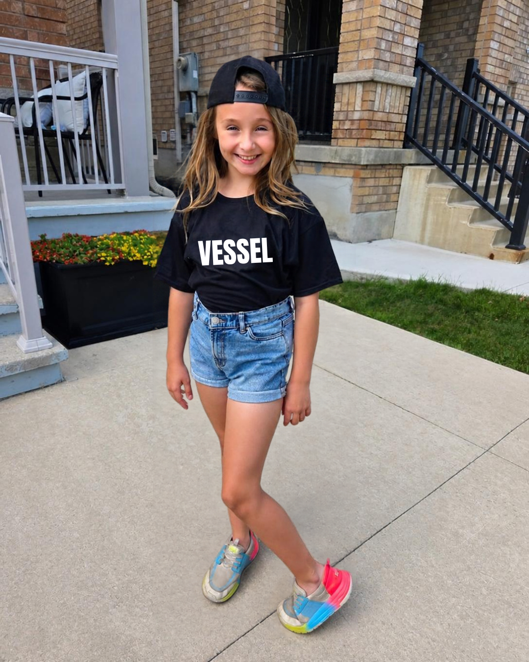 A child wearing a black Vessel T-shirt and cap
